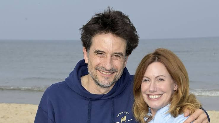 Katja Runge und Oliver Mommsen lächeln gemeinsam am Strand.