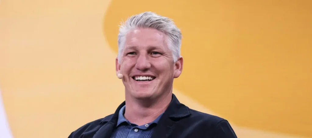 Bastian Schweinsteiger lächelt bei einem Bühnenauftritt vor gelbem Hintergrund