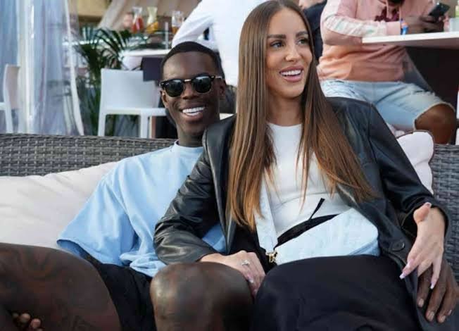 Ellen Ziolo und Dennis Schröder sitzen lachend nebeneinander auf einem Lounge-Sofa.